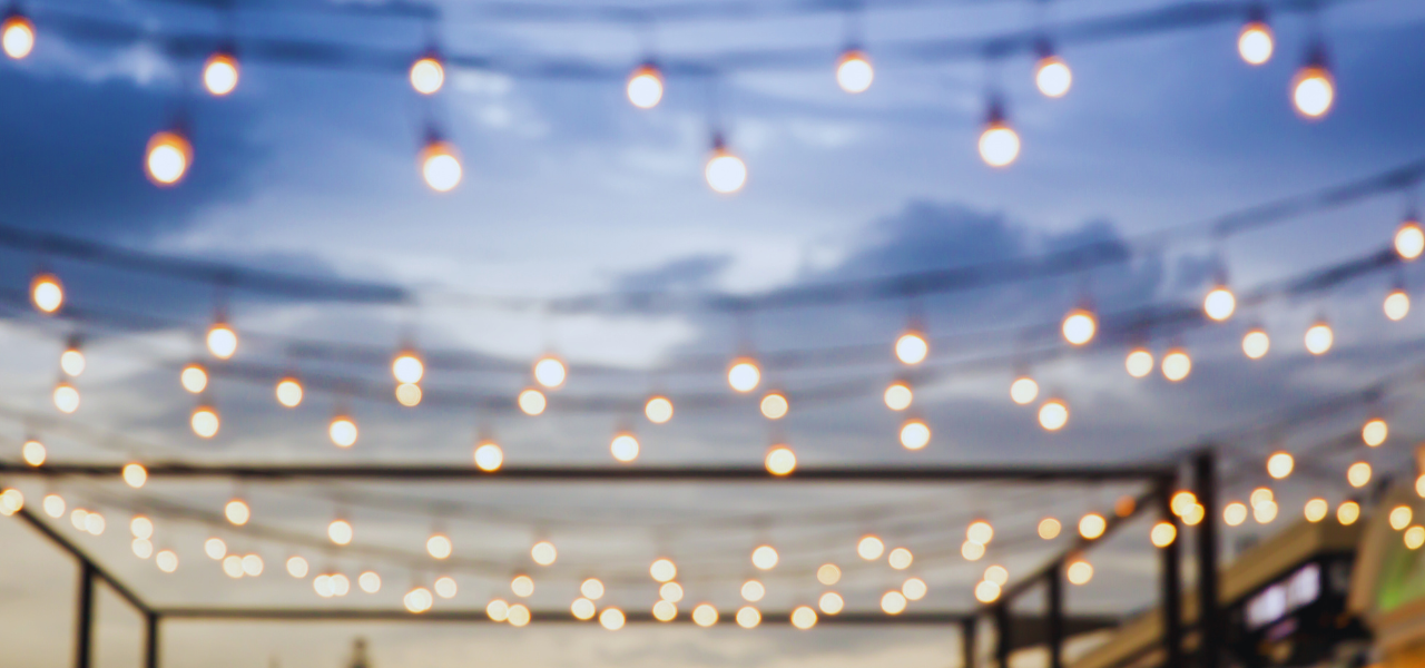 Multiple strings of fairy lights strung across a building during the evening.